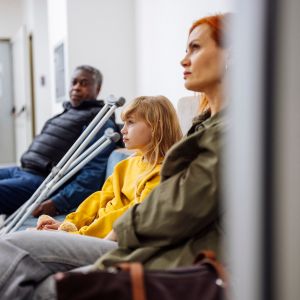 A family members with crutches are seated in a hospital waiting room, displaying expressions of worry and anticipation.